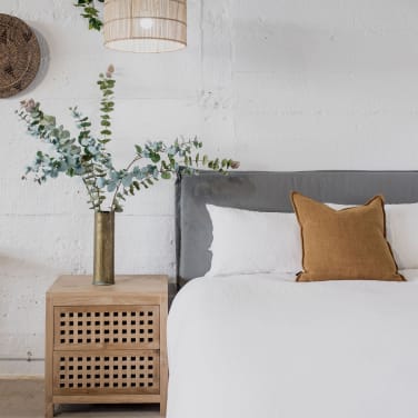 Image d’une chambre cosy avec une literie en lin et des lumières tamisées
Chambre chaleureuse avec une parure de lit en lin, des coussins en velours et une lampe en rotin pour une atmosphère douce et apaisante. une tête de lit en lin grise et une table de nuit en bois pour une ambiance cocooning et relaxante. 